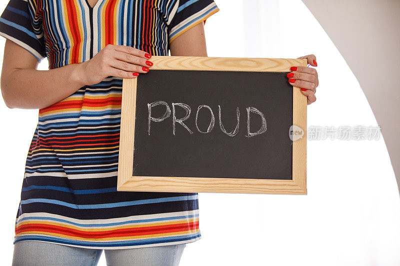 一个年轻的女人拿着一块写着"骄傲"的黑板。